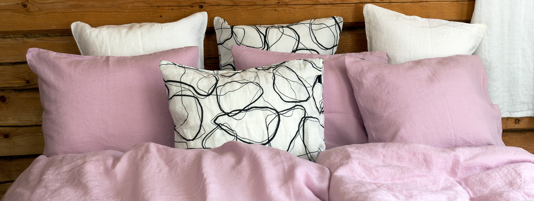 Vaaleanpunaisia tyynyjä sängyn päädyssä nojaamassa hirsiseinään